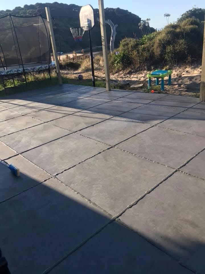 Completed decorative concrete area with square-cut control joints and grouted pattern, basketball hoop in the background, by Henwood Concrete