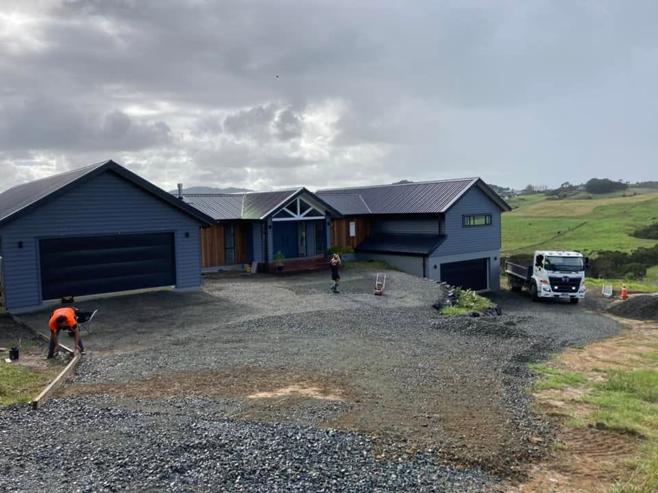 Large prepared and compacted basecourse area in front of a modern house, with a truck on the right and workers finishing the excavation and site preparation work by Henwood Concrete