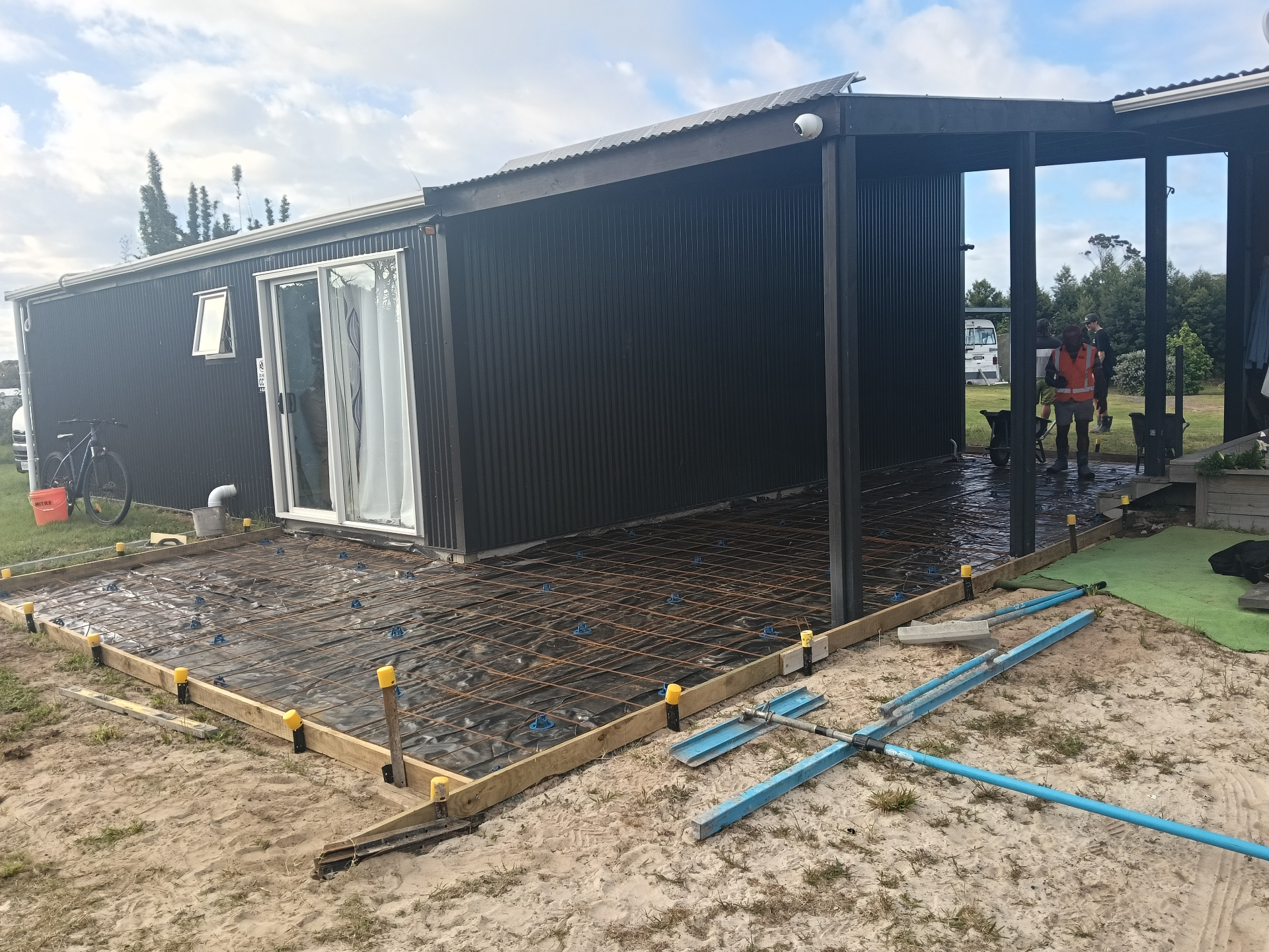 Large concrete area beside a black house with timber formwork, steel reinforcing mesh and blue chairs ready for the pour, by Henwood Concrete
